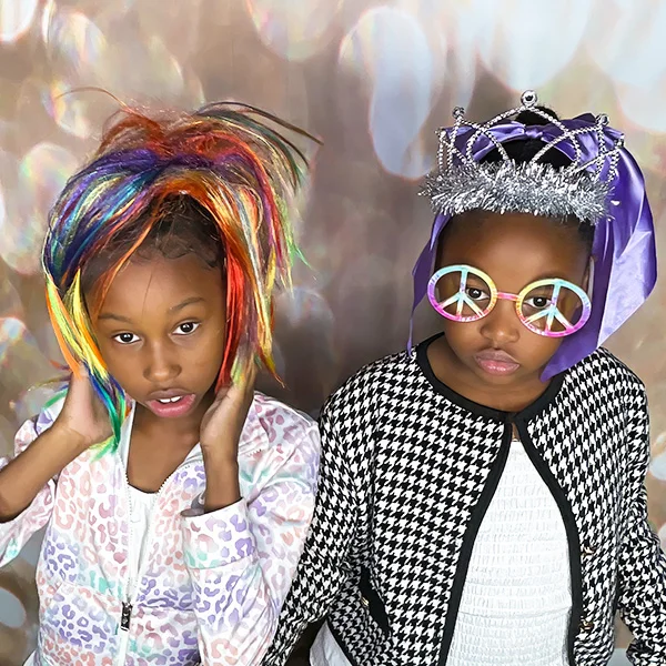 two young girls posing at photo booth wearing colorful wig princess tiara and peace sign glasses in Carson California