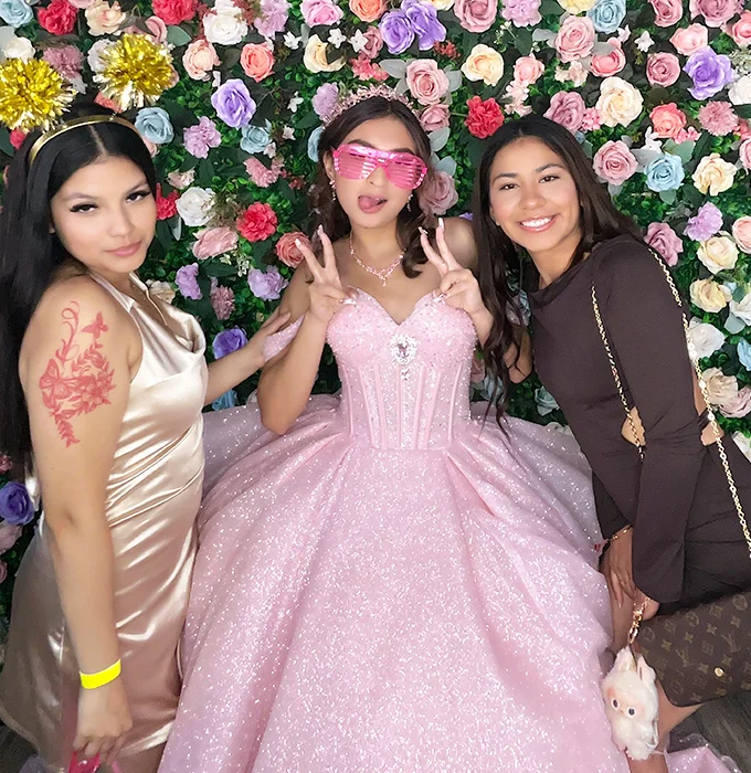 quinceanera girl in pink dress posing with friends at photo booth in Carson California holding plush toy and wearing pink glasses